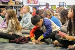 Elementary school students sitting on a carpeted floor folding origami paper