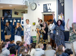 A group of teachers stand in a line performing a TikTok dance in front of students