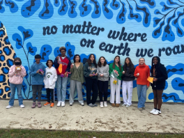 Group of middle school students stand in front of blue mural