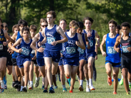A larger group of high school boys run in a group as they start a race.