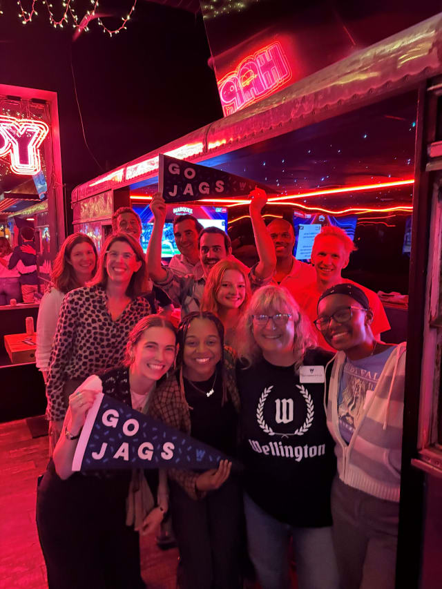 A group of adults stand in a red-lit bar