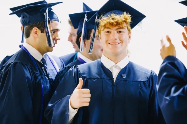 A high school senior stands in front of peers in a conversation smiling and giving a thumbs up