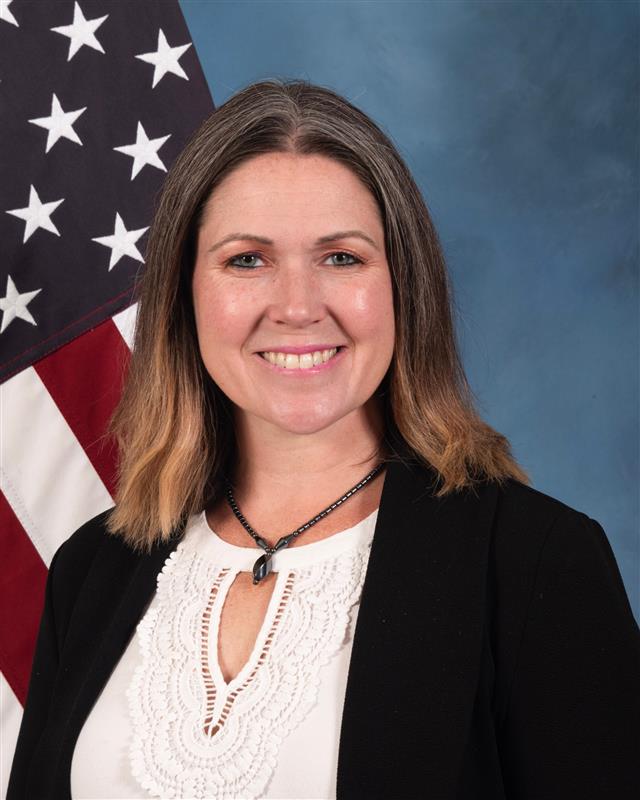 Woman poses in front of blue background and the flag of the United States