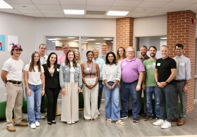 A group of smiling adults pose in a meeting workroom