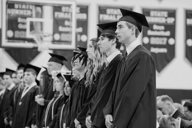 A black and white photograph of high school students standing in a line wearing graduation caps and gowns